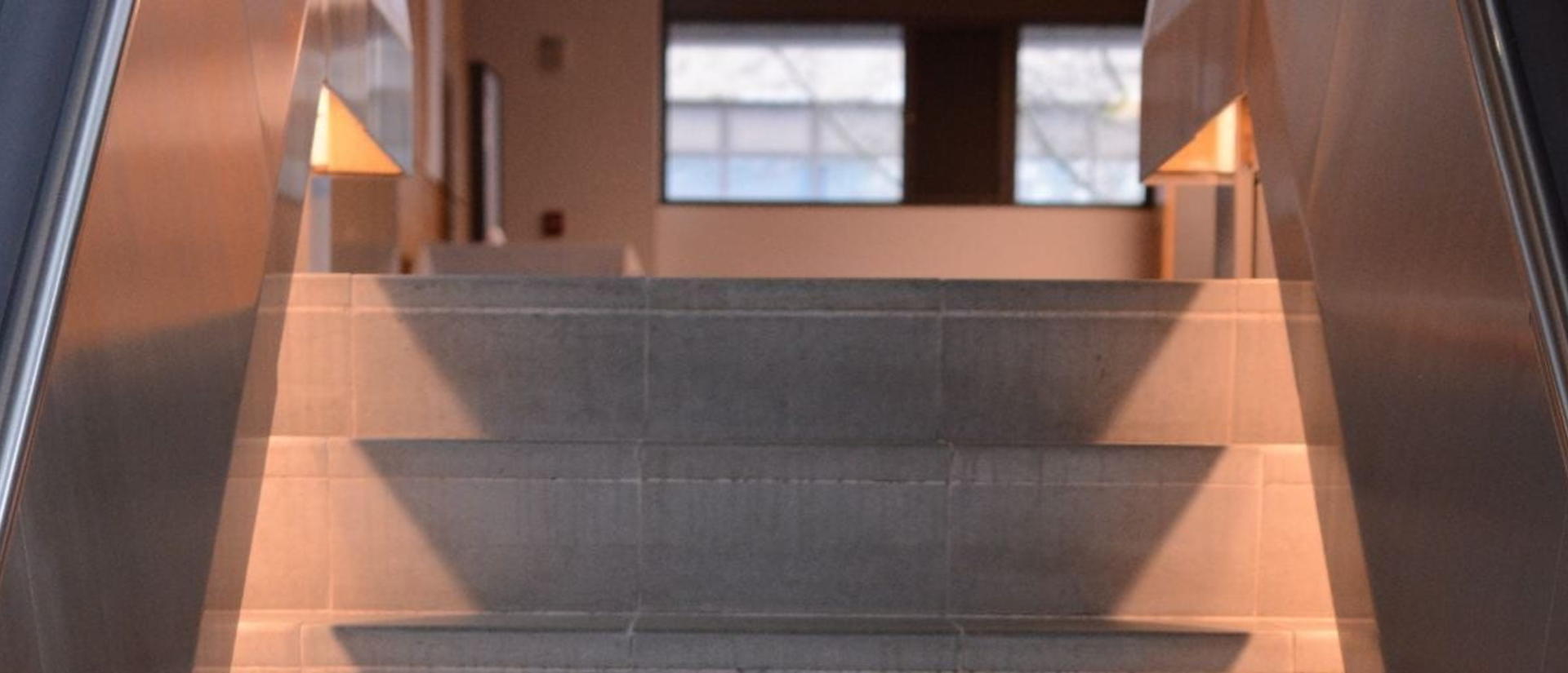 A stairway leading upward, illuminated by a bright light at the top, creating a warm and inviting atmosphere.