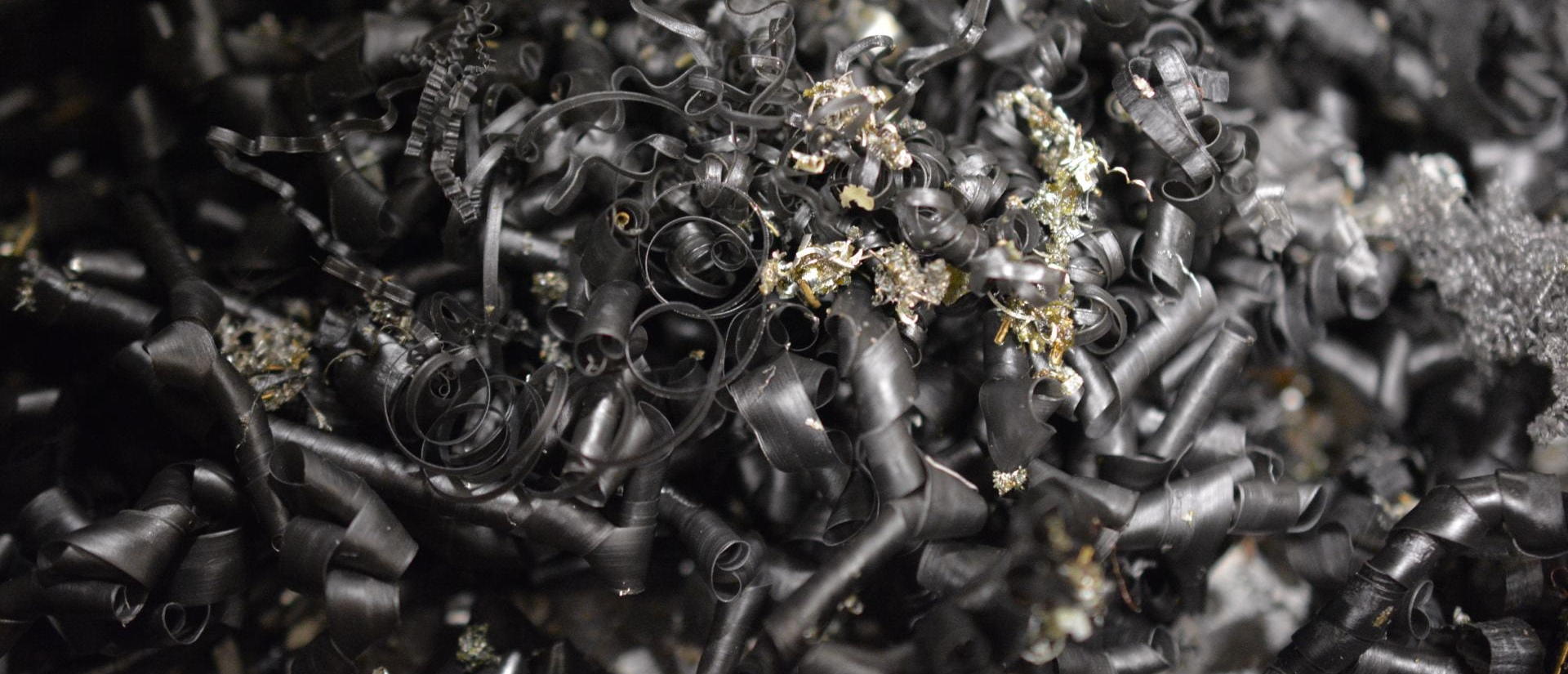 Curled metal shavings in shades of black and gray, with a few small pieces of gold-colored metal scattered throughout.